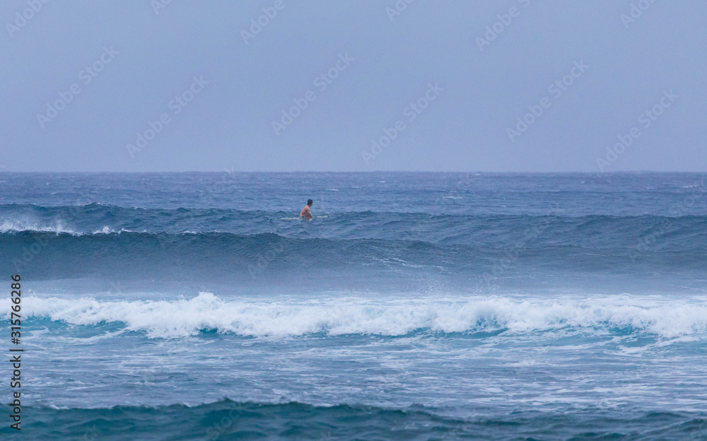 Lone surfer looking out to sea as he waits for waves in rough conditions