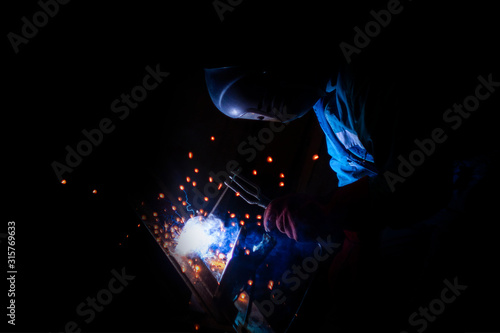 welder doing metal work at night, front and background blurred with bokeh effect © Torkhov