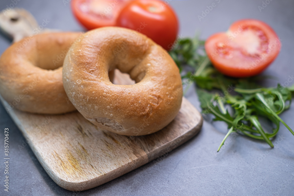 Bagels on a wooden table with tomatoes and rocket on background. Close up view. Bagels on a wooden table with tomatoes and rocket on background. Close up view.