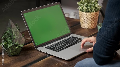 The person at the table is browsing the Internet on a green laptop screen. In a well-lit, cozy apartment. A man works in a loft office