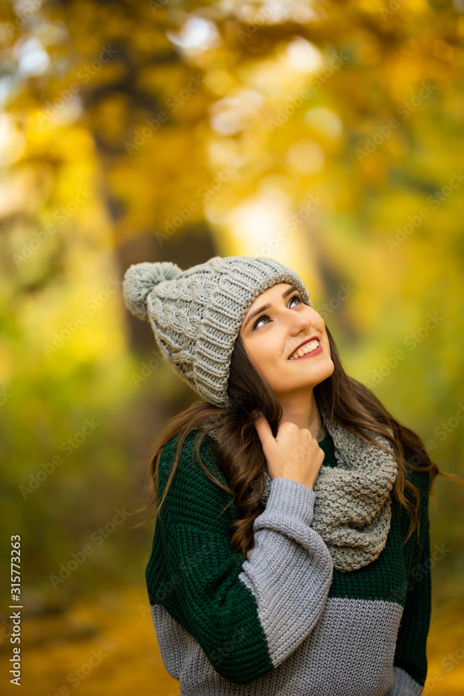 Photo of cute happy girl in autumnal park. Young woman wearing stylish hat and scarf in autumn park Photo of cute happy girl in autumnal park. Young woman wearing stylish hat and scarf in autumn park