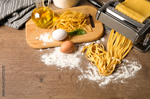 Pasta maker machine with dough and products on wooden table  above view