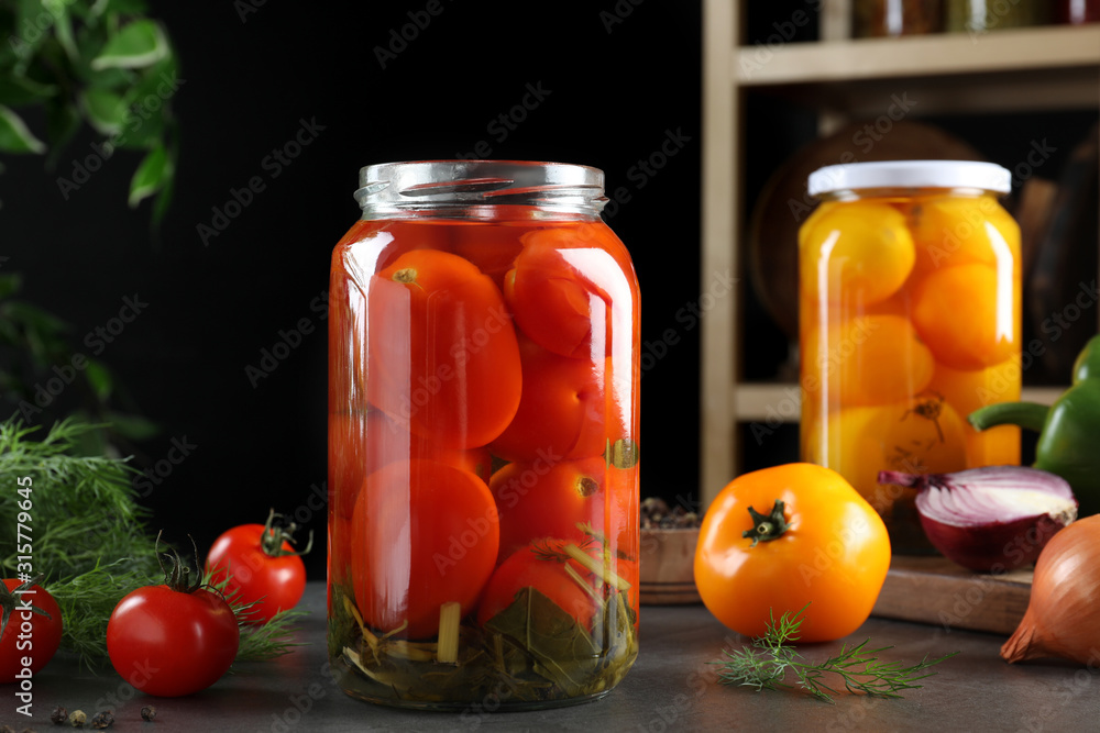 Glass jars of pickled tomatoes on grey table Glass jars of pickled tomatoes on grey table
