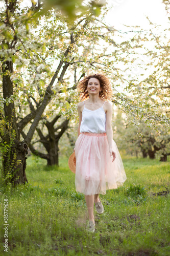 Young attractive woman with curly hair walking in a green flowered garden. Spring romantic mood © Kate