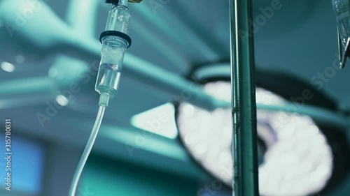 Intravenous drip in focus,surgeons team performing operation in the background,out of focus,infusion dripping.