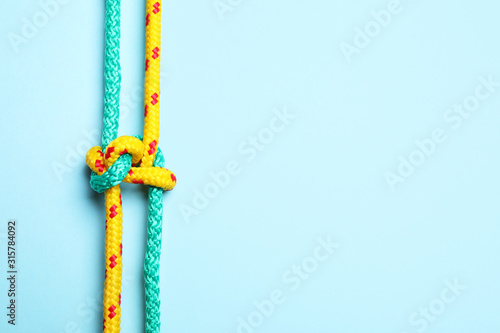 Top view of colorful ropes tied with knot on light blue background, space for text. Unity concept
