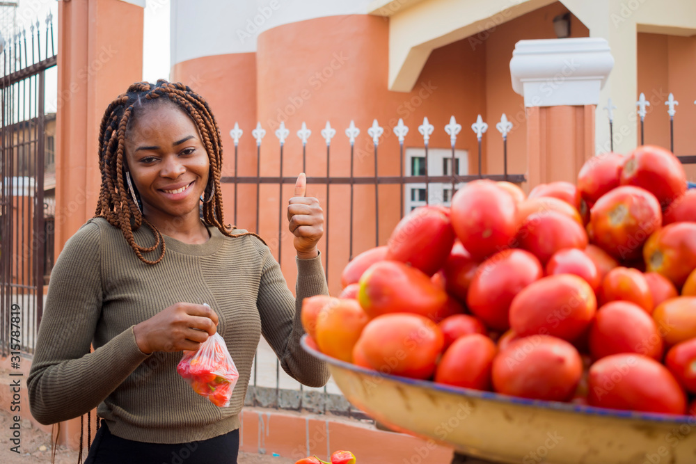 Φωτογραφία young beautiful market woman holding tomatoes in one hand and also did thumbs up with the other hand