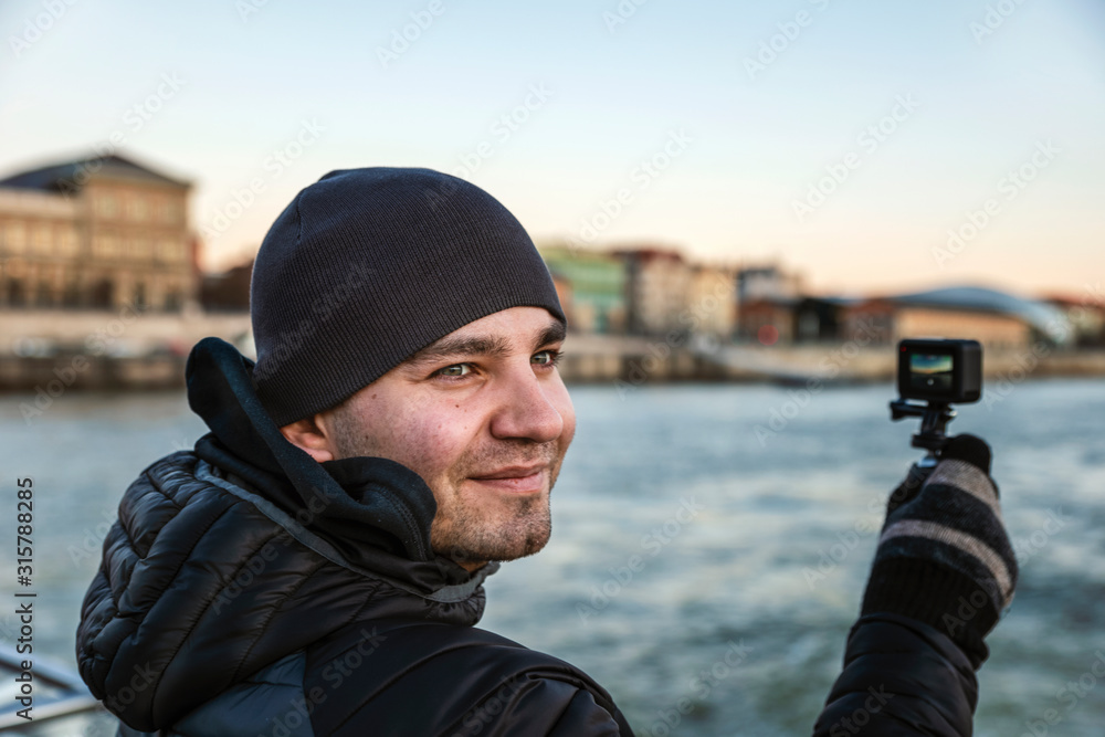 Happy frozen tourist shoots on an action camera of the Danube River surroundings in December. Happy frozen tourist shoots on an action camera of the Danube River surroundings in December.