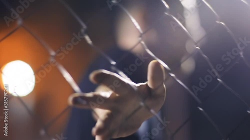 Helpless caucasian man touching and running fingers on metal fence feeling abandoned or imprizoned. Refugees and lack of freedom concept.