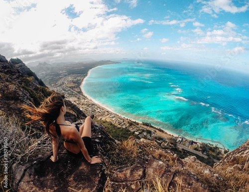 Woman sitting on top of rocky cliffs overlooking bright blue ocean, hair flowing in the wind © Cinestock