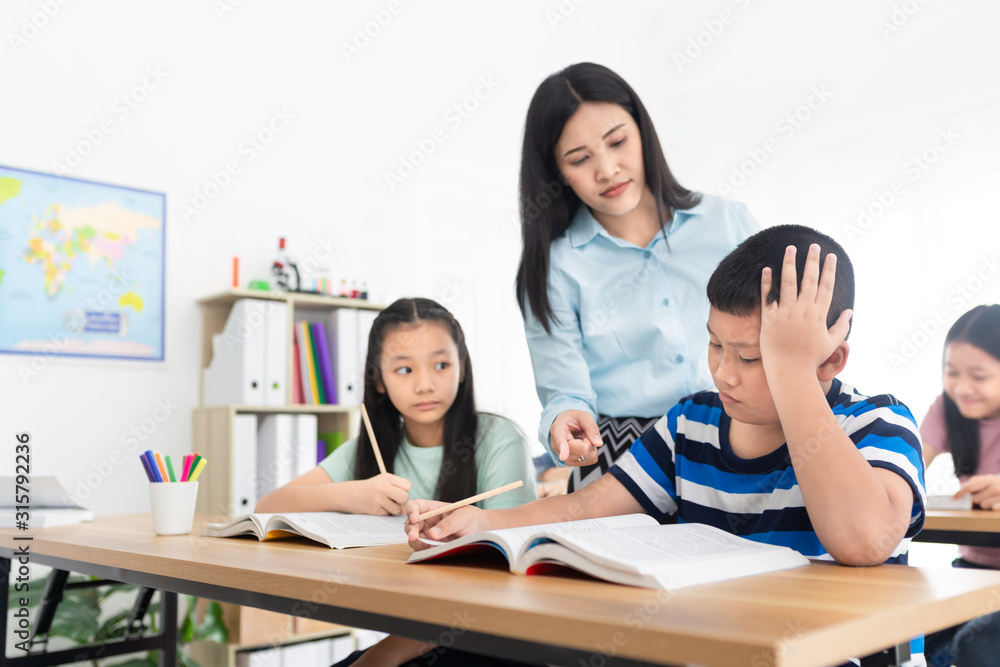 asian students studying and do work with teacher in classroom, asian teacher teaching and explaining about how to do homework, asian boy feeling stress and headaches, happiness elementary school asian students studying and do work with teacher in classroom, asian teacher teaching and explaining about how to do homework, asian boy feeling stress and headaches, happiness elementary school
