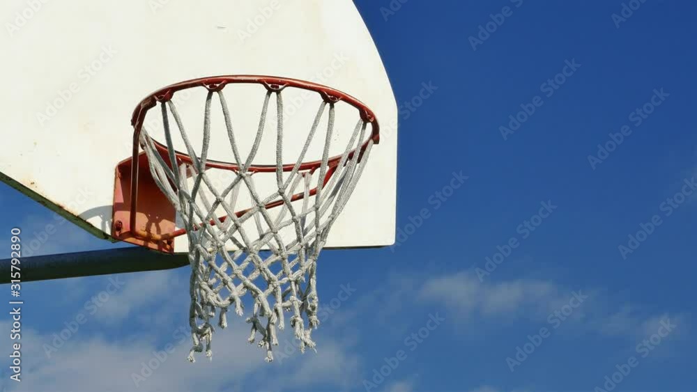 Basketball net in a wooden basketball hoop with blue sky and clouds close up Basketball net in a wooden basketball hoop with blue sky and clouds close up