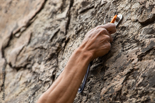 A close up view of advanced rock climbing gear in use as the hand of a man grabs onto a secured belay device, health and safety during risky sport