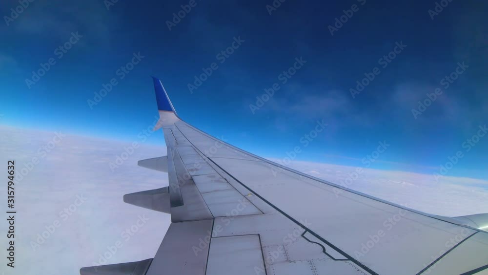 Wispy clouds float past the windows of an airplane just above the wing. Blue skies above and a pillow of clouds below. Traveling on a nice day. Wispy clouds float past the windows of an airplane just above the wing. Blue skies above and a pillow of clouds below. Traveling on a nice day.
