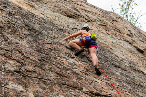A low angle shot of an advanced lady rock climber scaling a steep crag with rope and harness, anchoring safety equipment to rock. With copy space
