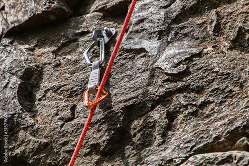 A close up and detailed view of a belay device and dynamic rope secured to a rugged limestone cliff. Professional rock climbing equipment in use