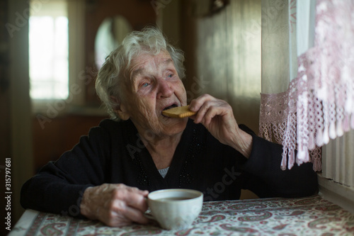 An elderly woman drinking tea with cookies at home.