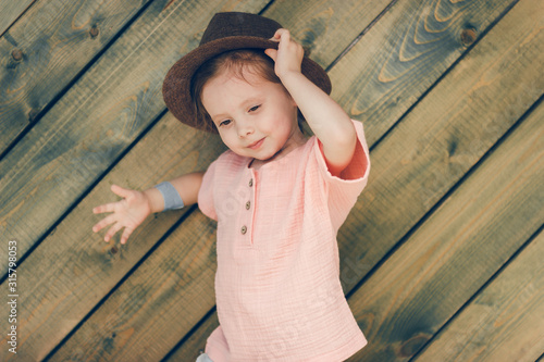 Portrait of happy cute little girl in rural style brown hat and muslin clothes in a summer day on green wooden background.