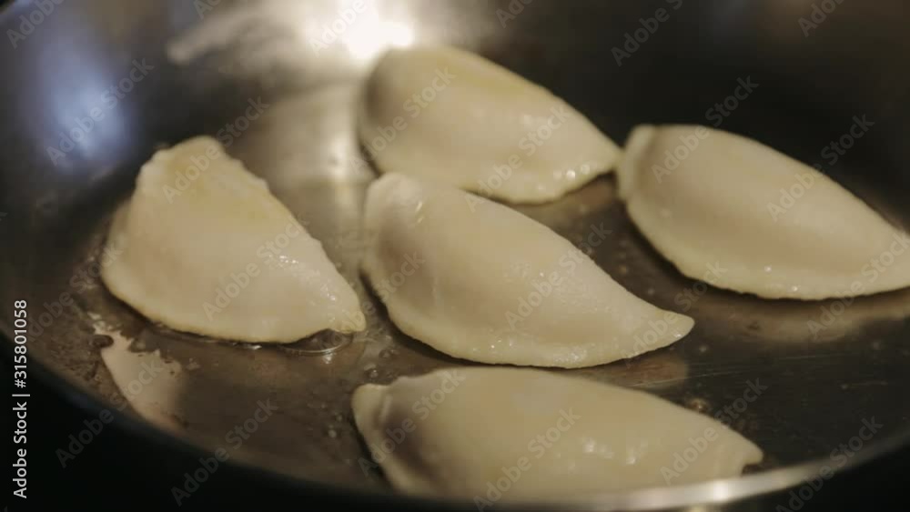 Canada - Frying Five Dumplings In A Stainless Pan With Cooking Oil Using Tongs - Closeup Shot Canada - Frying Five Dumplings In A Stainless Pan With Cooking Oil Using Tongs - Closeup Shot