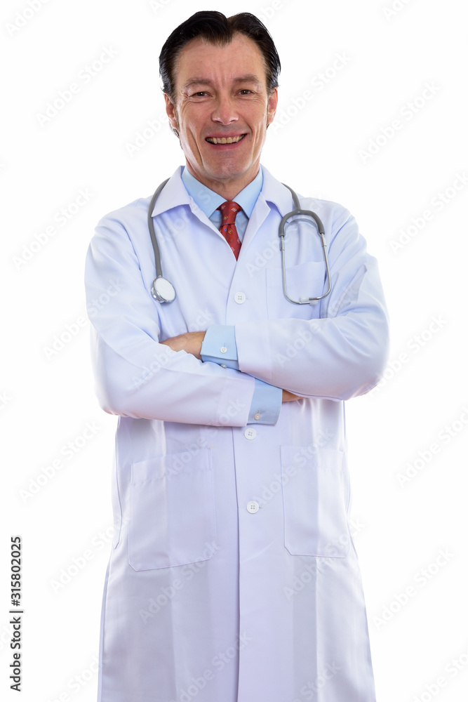 Studio shot of mature happy man doctor standing and smiling with arms crossed Studio shot of mature happy man doctor standing and smiling with arms crossed