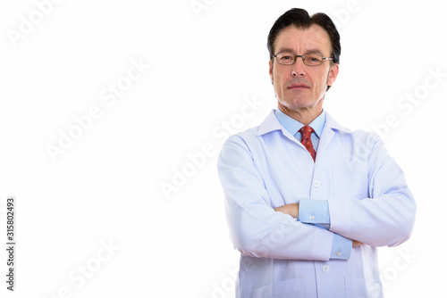 Studio shot of mature handsome man doctor wearing eyeglasses with arms crossed © Ranta Images