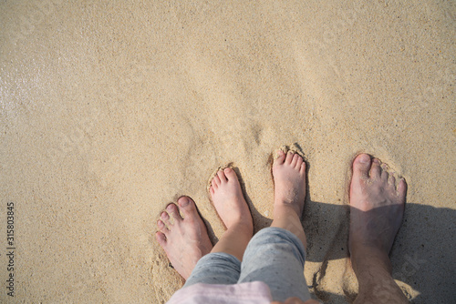 Father and child stand barefoot on the beach.