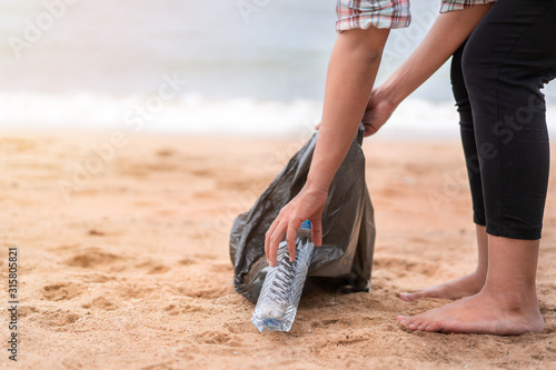 Asian woman picking bottle into plastic bag black for cleaning the beach in morning time, Volunteer concept.