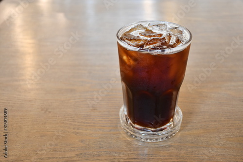 A glass of ice Americano on wooden table in cafe.