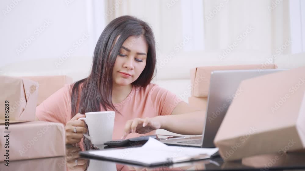Pretty online shop owner working with laptop while drinking a cup of hot coffee in the living room at home. Shot in 4k resolution Pretty online shop owner working with laptop while drinking a cup of hot coffee in the living room at home. Shot in 4k resolution