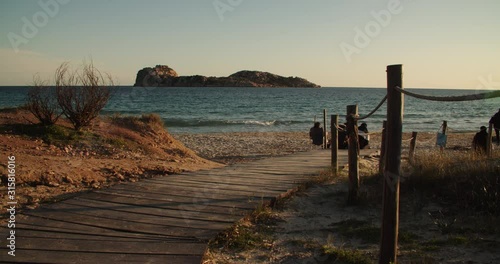 Wooden walkway at beach with people in front of island, sunset, Porto Tramatzu