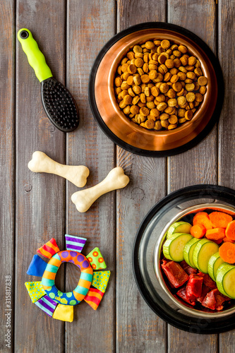 Dog feed - dry food and raw meat - near toy, brush and cheving bones ondark wooden background top view photo