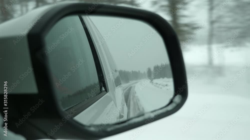 Snowy road and twinkling pine forest reflected in a car side mirror in Finland Snowy road and twinkling pine forest reflected in a car side mirror in Finland