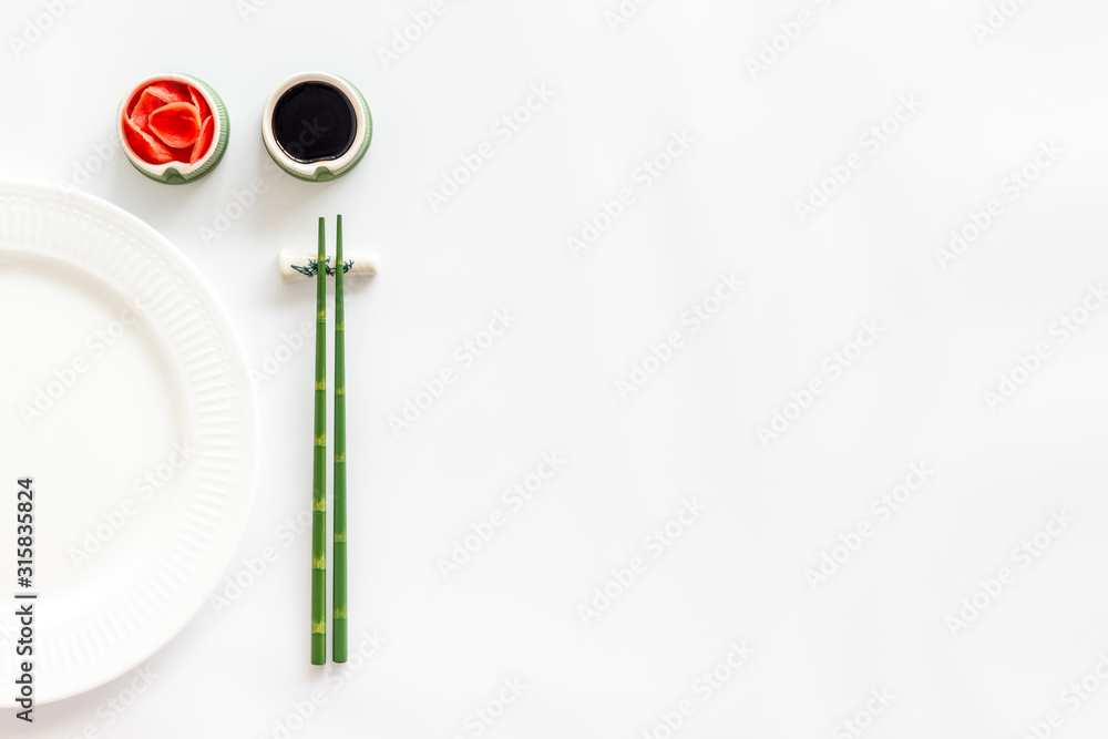Tableware for sushi and rolls. Plate, chopsticks, small bowls with ginger and sause on white background top-down copy space Tableware for sushi and rolls. Plate, chopsticks, small bowls with ginger and sause on white background top-down copy space