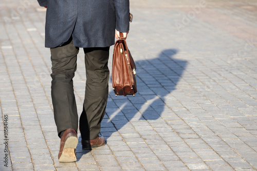 Man in a business suit carrying leather briefcase walking on the street, shadow on a pavement. Concept of official, businessman, politician, career advancement