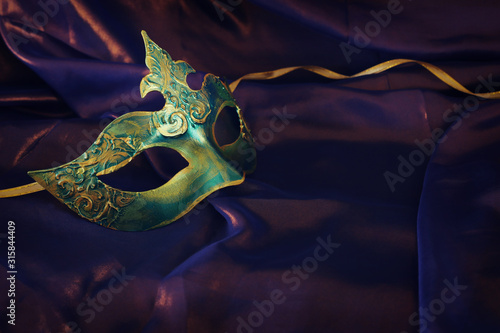 Photo of elegant and delicate gold and green Venetian mask over purple silk background