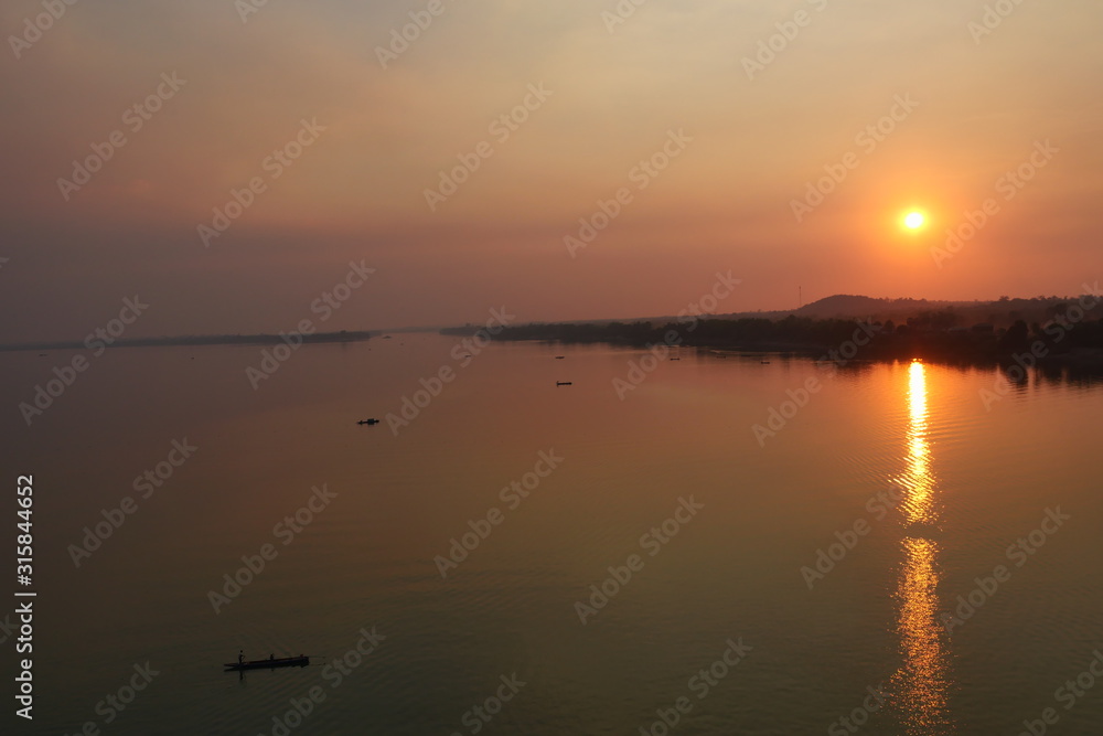 Aerial view  view of the Mekong River at sunset, The silhouette of small fishing boat with forest and orange  sun on red sky reflecting on the water surface at dusk, Stung Treng, Cambodia