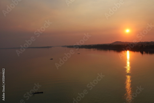 Aerial view view of the Mekong River at sunset, The silhouette of small fishing boat with forest and orange sun on red sky reflecting on the water surface at dusk, Stung Treng, Cambodia