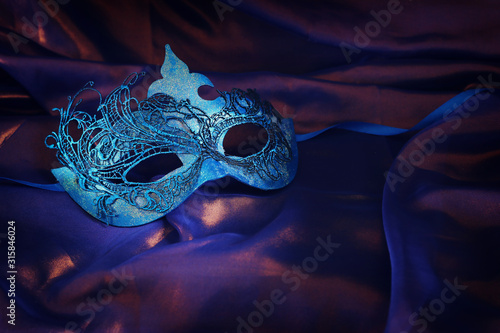 Photo of elegant and delicate blue Venetian mask over purple silk background