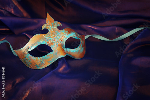 Photo of elegant and delicate blue and bronze Venetian mask over purple silk background