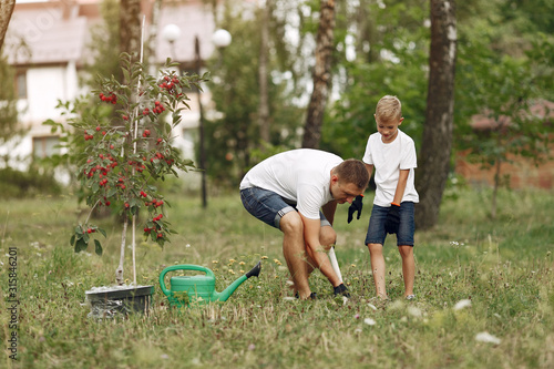 Family on a yard. Father with son planting a tree. Boy with a green funnel