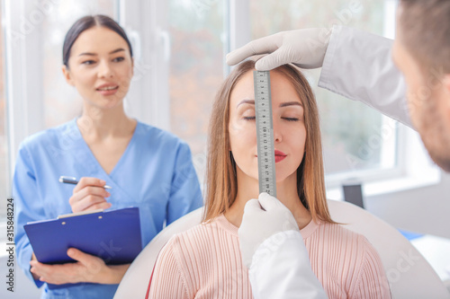 Foto Plastic surgeon examining young woman's face prior to operation in clinic