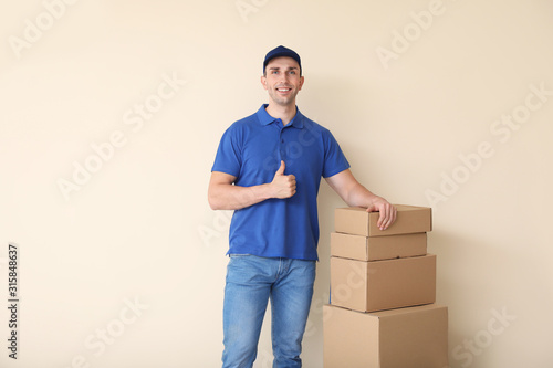 Delivery man with boxes showing thumb-up on color background