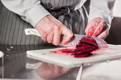 Closeup of hand with knife cutting fresh vegetable. Young chef cutting beet on a white cutting board closeup. Cooking in a restaurant kitchen