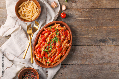 Plate with tasty pasta and tomato sauce on wooden table