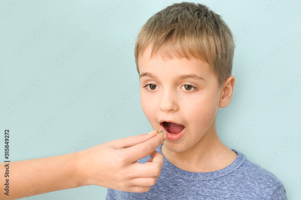Mother giving little son fish oil pill against color background Mother giving little son fish oil pill against color background