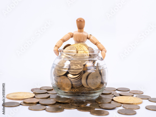 Miniature wooden figure sits on spilled jar with coins. Business concept with coins.