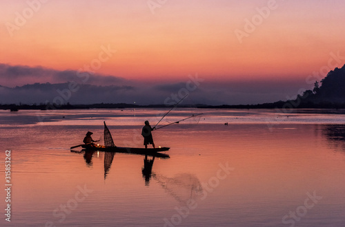 Silhouette of fisherman on wooden boat in nature lake with sunrise © Sasint