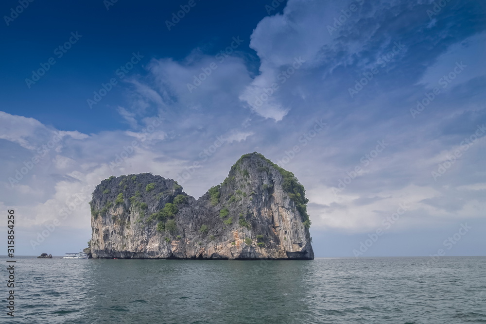 view of high rock cliff, Ko Mar (horse island) in the sea with cloudy sky background, Trang sea, southern of Thailand.