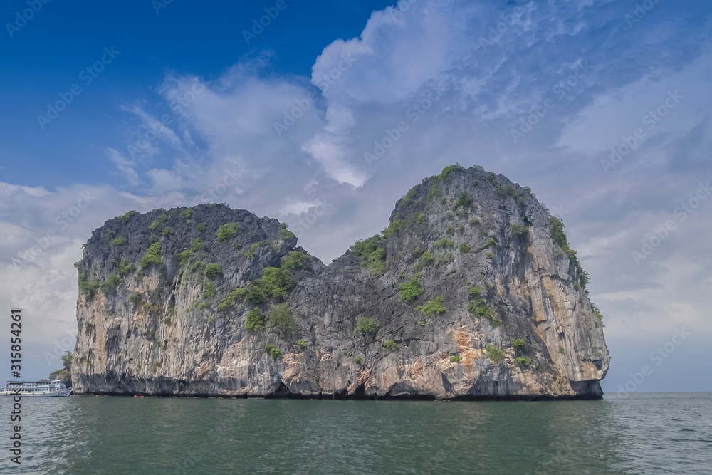 view of high rock cliff, Ko Mar (horse island) in the sea with cloudy sky background, Trang sea, southern of Thailand.
