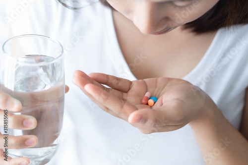 Closeup woman hand holding pills and glass of water  health care and medical concept  selective focus